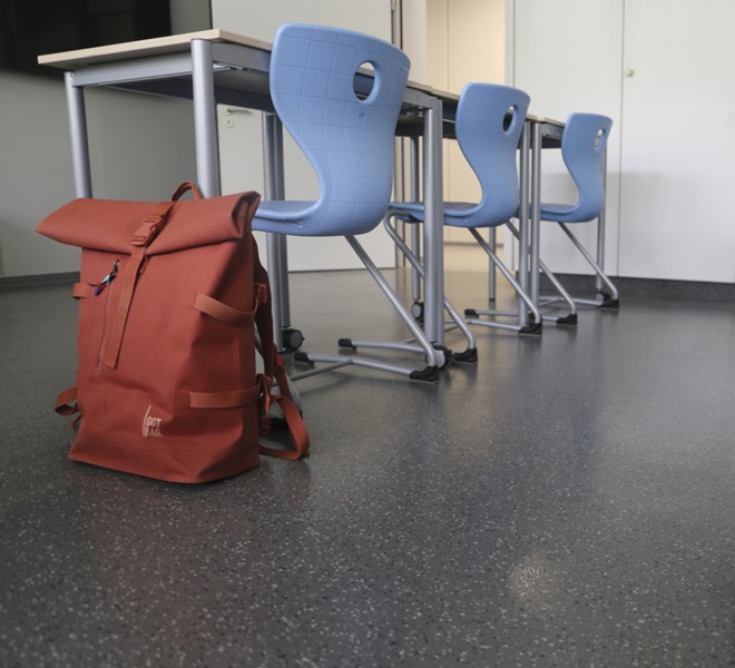 Tischreihe, davor eine Tasche in Berufsschul-Klassenzimmer. Der anthrazitfarbene Boden norament 926 grano nTx hat eine schnelle und risikoarme Sanierung ermöglicht