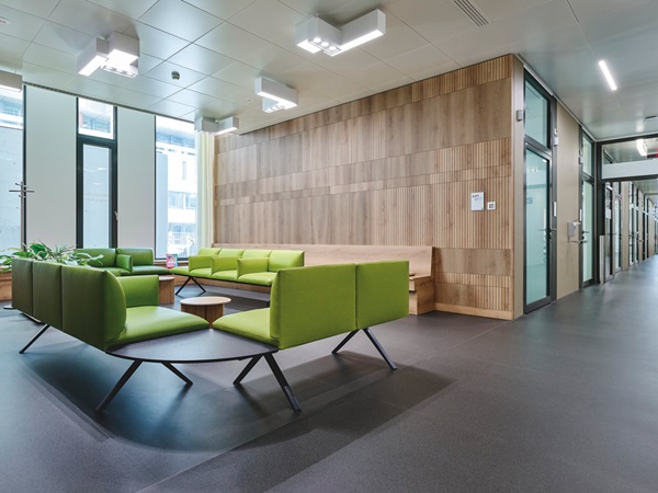 Waiting area in hospital with wooden walls and benches, dark floor and green seat cushions