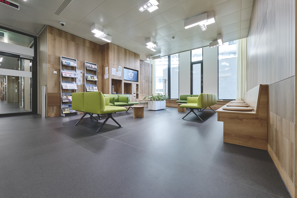 Wartebereich im Spital, Holz, der dunkle Boden noracare seneo und grüne Sitzpolster prägen das Ambiente